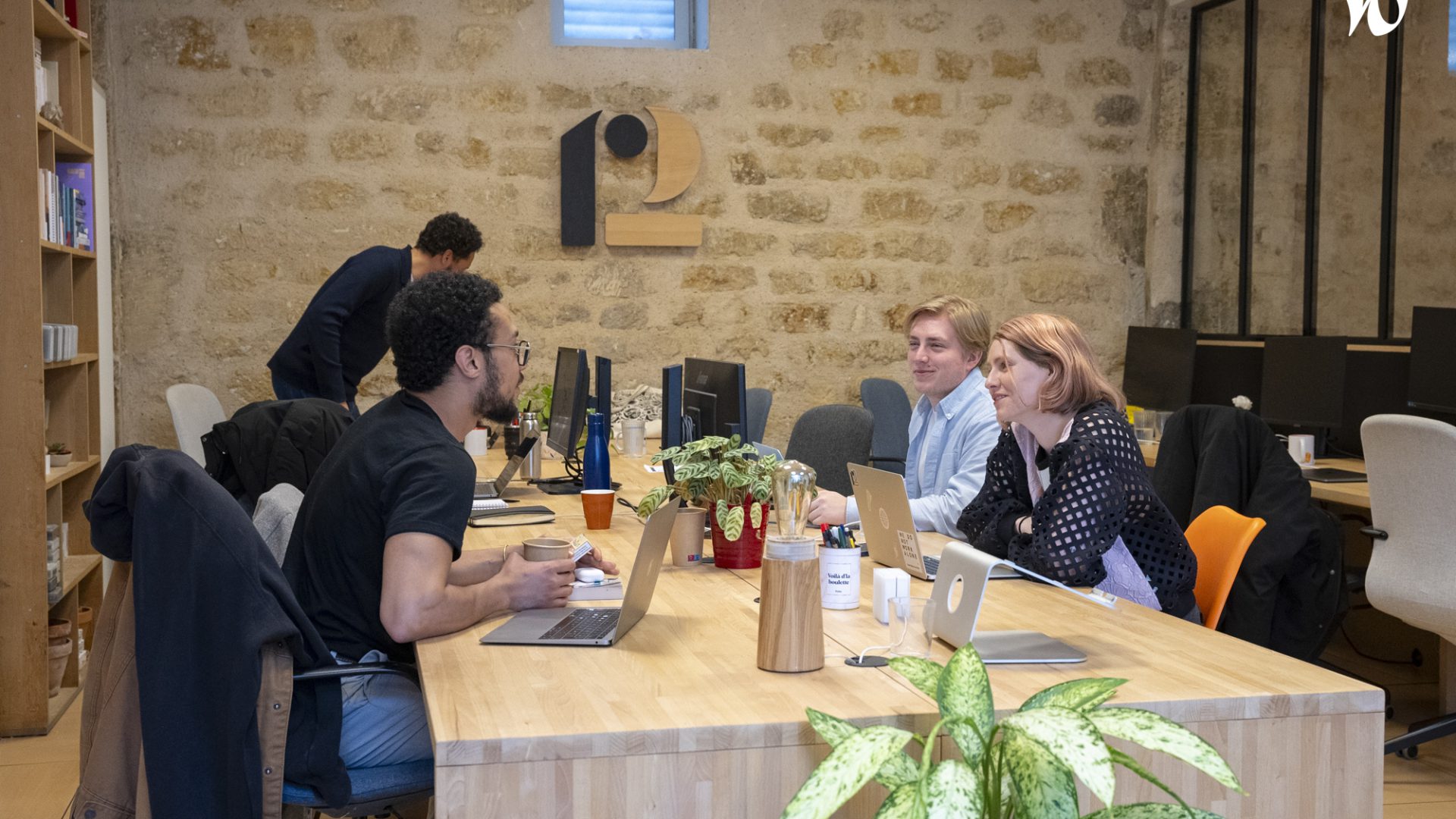 Des personnes échangeant et travaillant ensemble dans un espace de bureau moderne et décontracté avec des plantes et des ordinateurs.