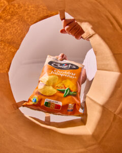 Un paquet de chips au goût cheddar jalapeño est visible, pris par une main à travers une ouverture en papier.