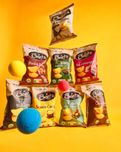 Une variété de paquets de chips Brets aux saveurs différentes est disposée sur un fond jaune, accompagnée de boules colorées flottantes.